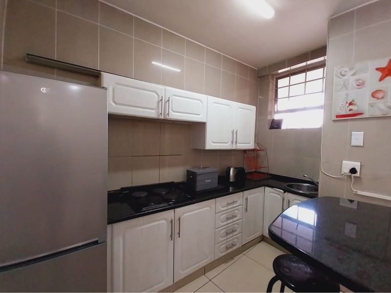 Compact kitchen featuring white cabinetry, dark granite countertops, tiled walls, and a built-in hob, providing a functional workspace.