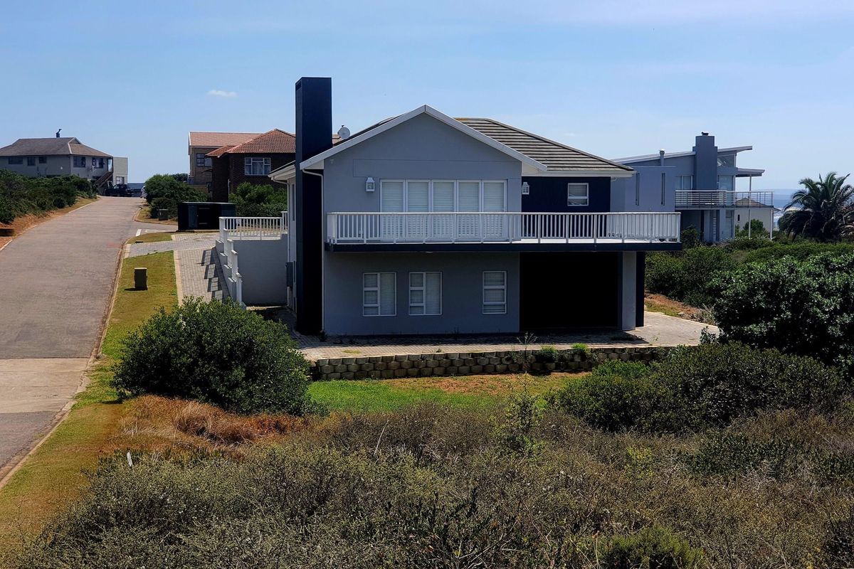 An elevated view of a modern two-story residential property featuring a balcony, paved driveway, and established landscaping in a coastal neighborhood setting.