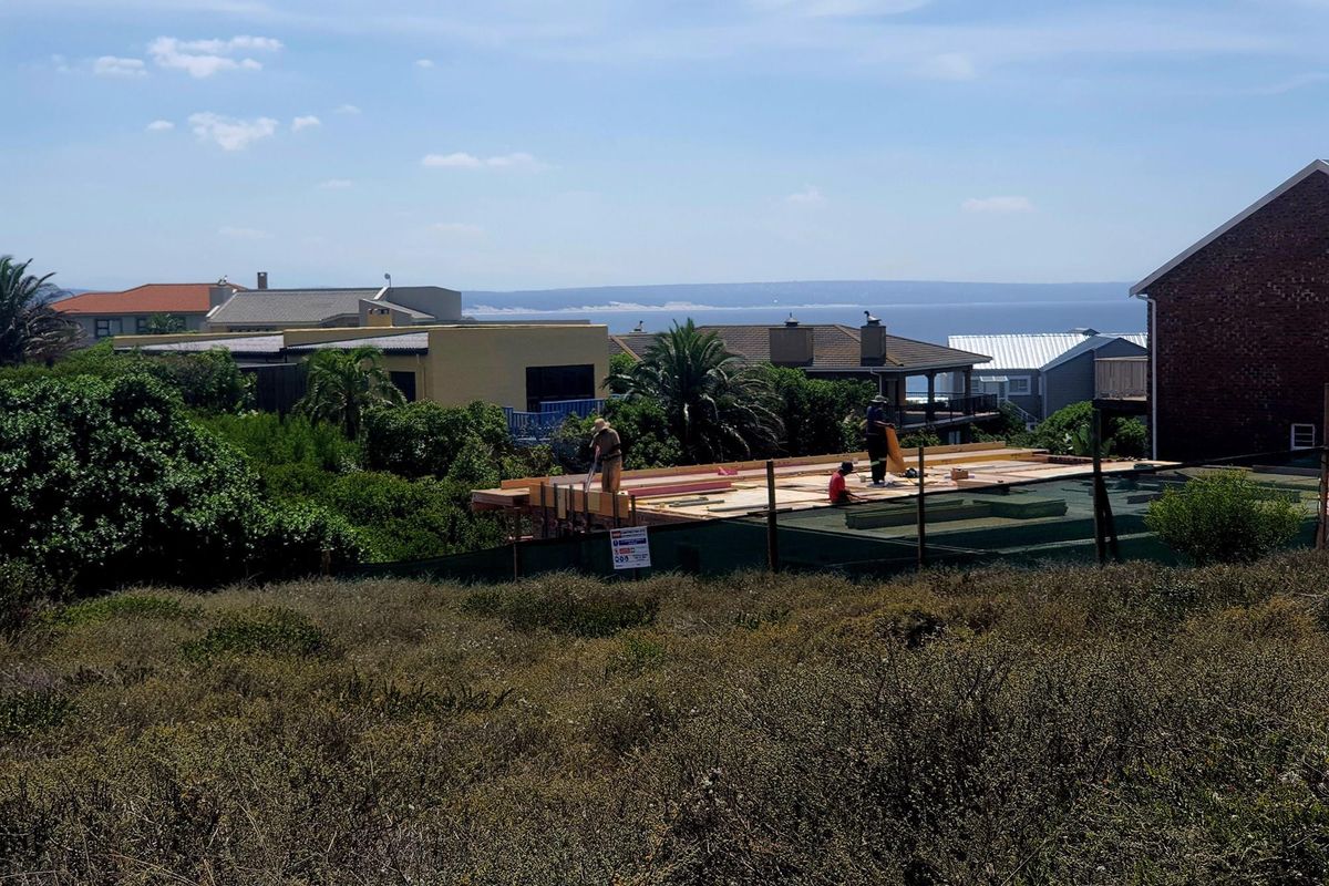 A view of a residential construction site on a vacant plot, featuring ongoing structural work with a coastal backdrop.