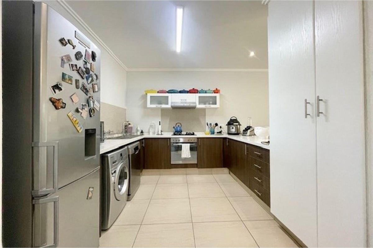 A functional U-shaped kitchen featuring dark wood cabinetry, light countertops, tiled flooring, and integrated space for laundry appliances.