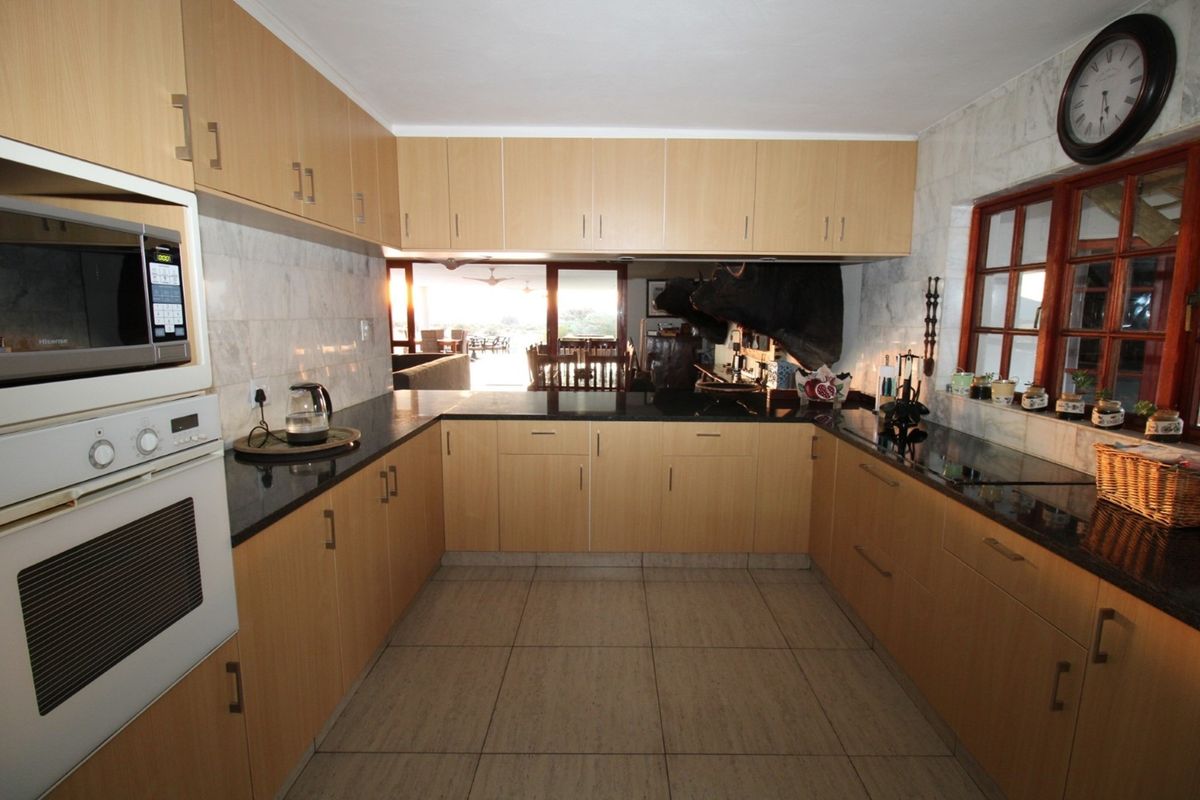 A functional U-shaped kitchen featuring light wood cabinetry, dark granite countertops, tiled flooring, and a built-in oven and microwave unit.