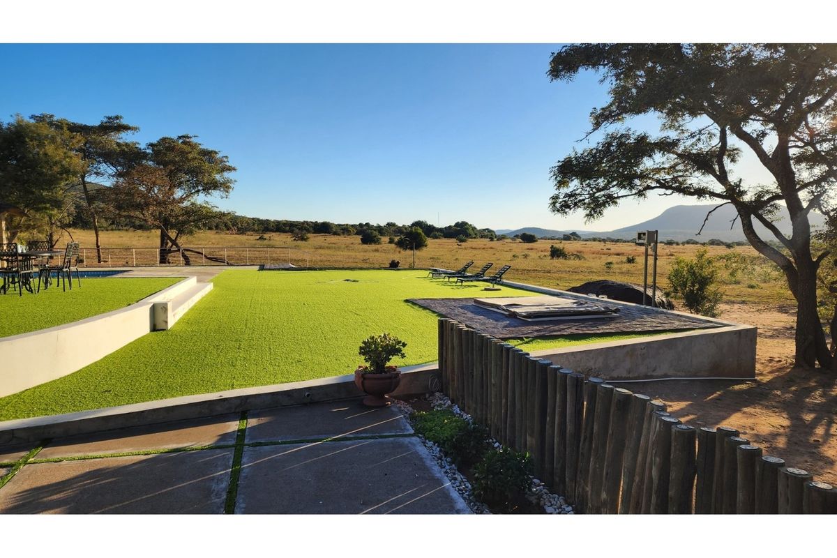 Spacious outdoor entertainment area featuring artificial lawn, concrete retaining walls, and a raised deck area overlooking the natural landscape.