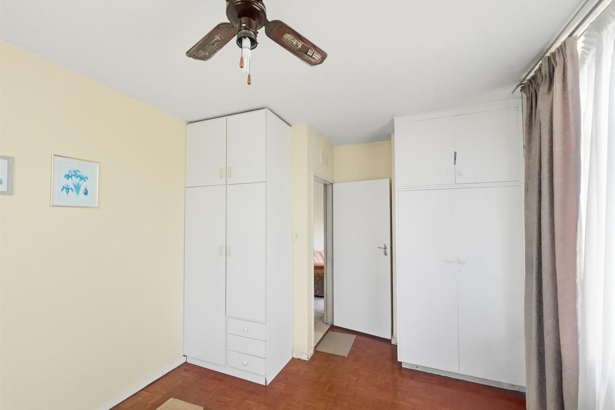 A bedroom featuring built-in white cabinetry, parquet flooring, and a ceiling fan, offering functional storage space.