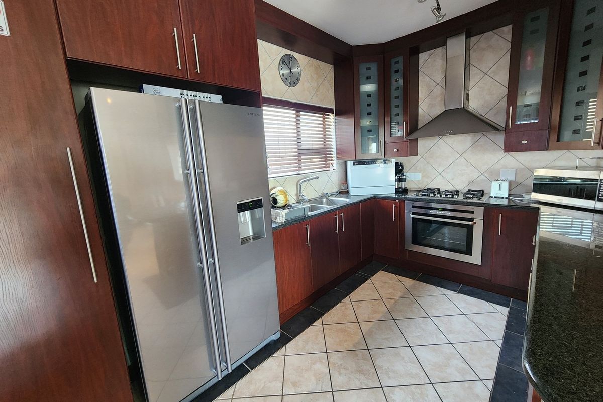 A functional kitchen featuring dark wood cabinetry, granite countertops, tiled backsplash, and built-in stainless steel appliances including an oven and extractor fan.