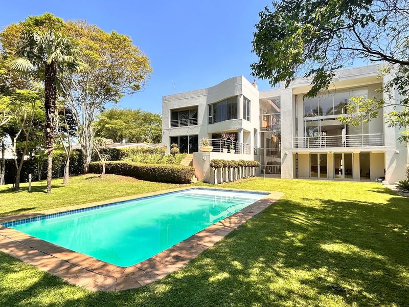 A spacious multi-level residence featuring a large swimming pool, landscaped garden, and expansive glass windows overlooking the rear outdoor entertainment area.