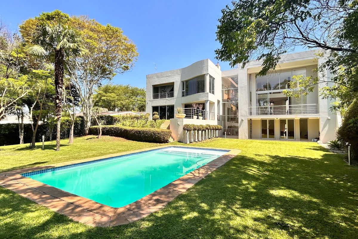 A spacious multi-level residence featuring a large swimming pool, landscaped garden, and expansive glass windows overlooking the rear outdoor entertainment area.