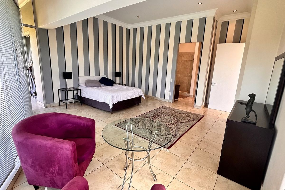 Spacious bedroom featuring tiled flooring, striped accent walls, and an en-suite bathroom access, offering a comfortable and well-defined living space.
