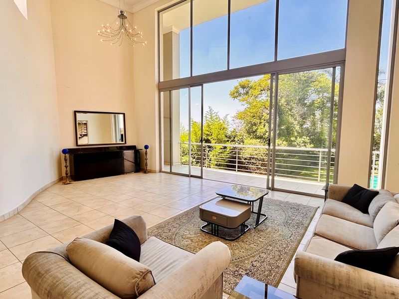 Spacious double-volume living area featuring large floor-to-ceiling windows and sliding doors that open onto a private balcony with garden views.