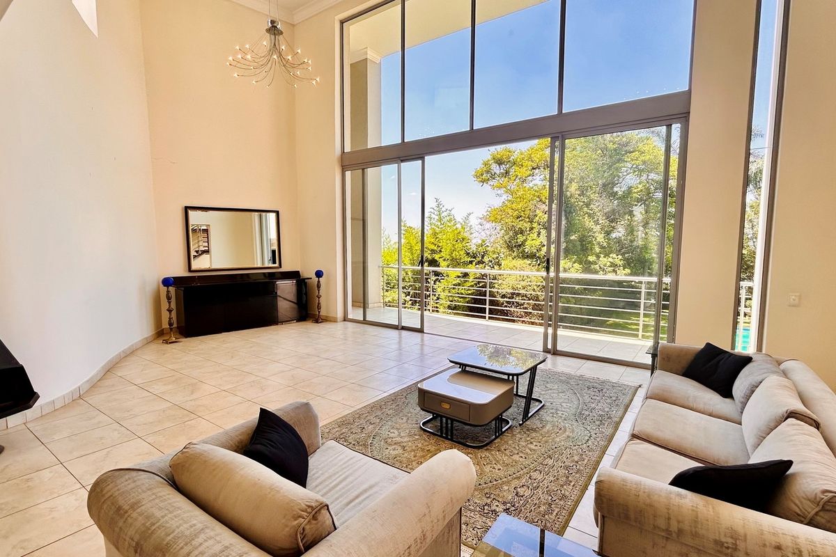 Spacious double-volume living area featuring large floor-to-ceiling windows and sliding doors that open onto a private balcony with garden views.