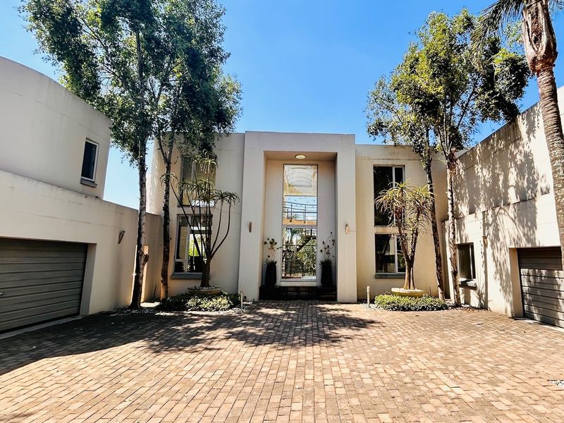 Modern architectural front facade featuring a paved driveway, double garage, and a prominent central glass entrance with mature trees.