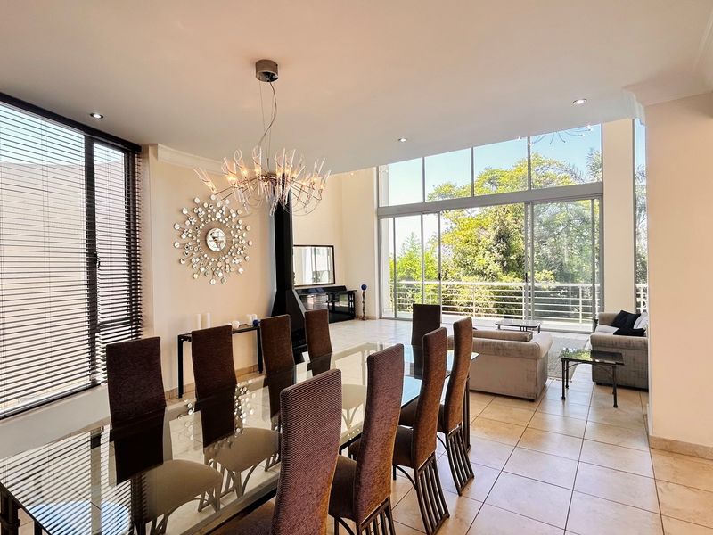 Spacious open-plan living and dining area featuring high ceilings, large floor-to-ceiling windows, a modern fireplace, and direct access to a balcony with garden views.