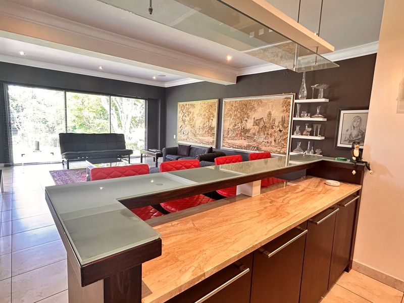 Spacious open-plan living area featuring a built-in bar with stone countertop, glass shelving, and large sliding doors leading to the outdoor space.