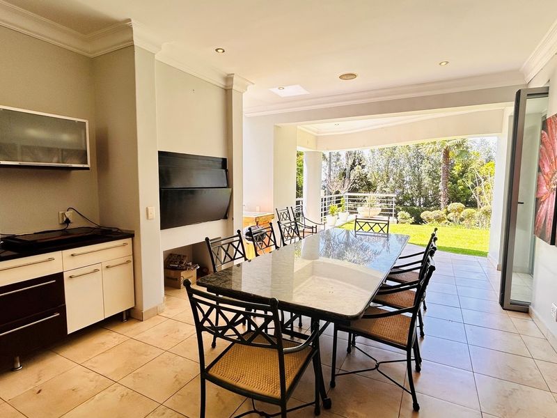 Spacious open-plan dining and entertainment area featuring a built-in braai, tiled flooring, and seamless flow to a covered patio and garden.