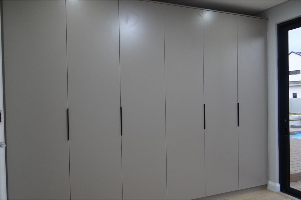 A bedroom featuring modern, floor-to-ceiling built-in cupboards with sleek matte grey finish and minimalist black handles.
