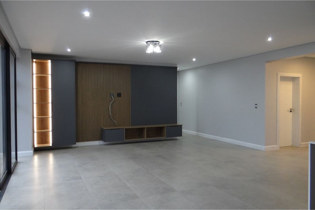 Modern living area featuring large format floor tiles, recessed downlighting, and a custom built-in media wall with timber slat detailing and integrated shelving.