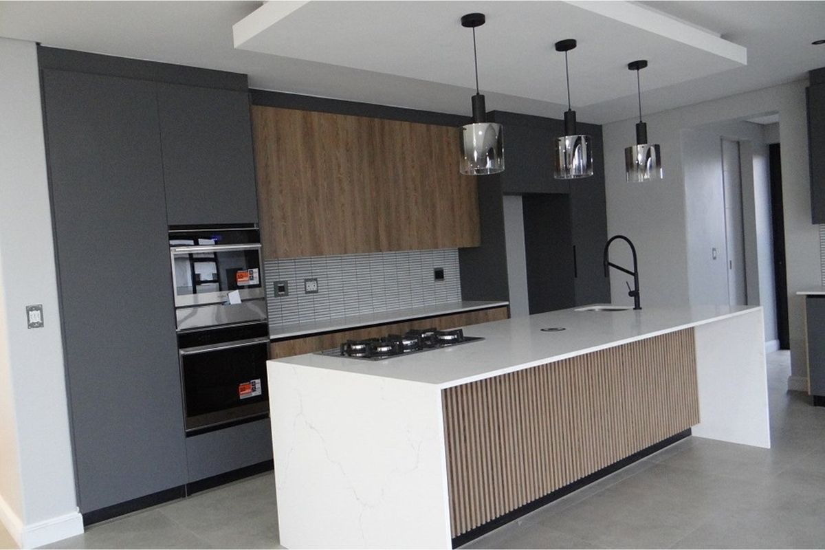 Modern kitchen featuring a large central island with stone countertops, integrated gas hob, built-in double ovens, and contemporary cabinetry with wood-look accents.