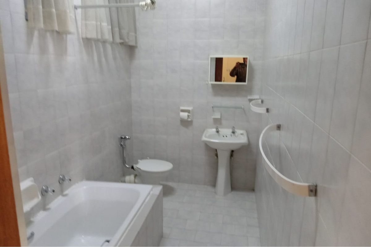A functional bathroom featuring a pedestal sink, bathtub, and toilet, finished with neutral wall and floor tiling.