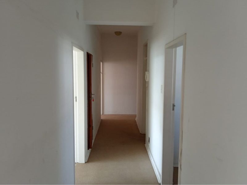 A vacant apartment hallway featuring neutral walls, carpeted flooring, and an integrated intercom system, providing access to multiple rooms.