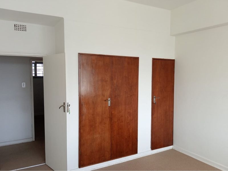 An empty bedroom featuring built-in wooden cupboards and neutral carpeted flooring, offering a blank canvas for personalization.