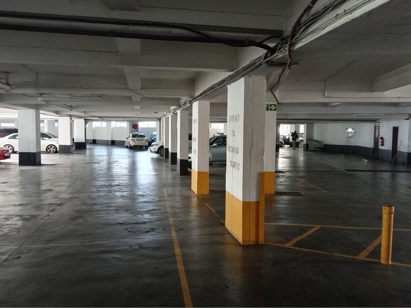 A functional underground parking garage featuring concrete structural columns, painted flooring with marked bays, and overhead utility services.