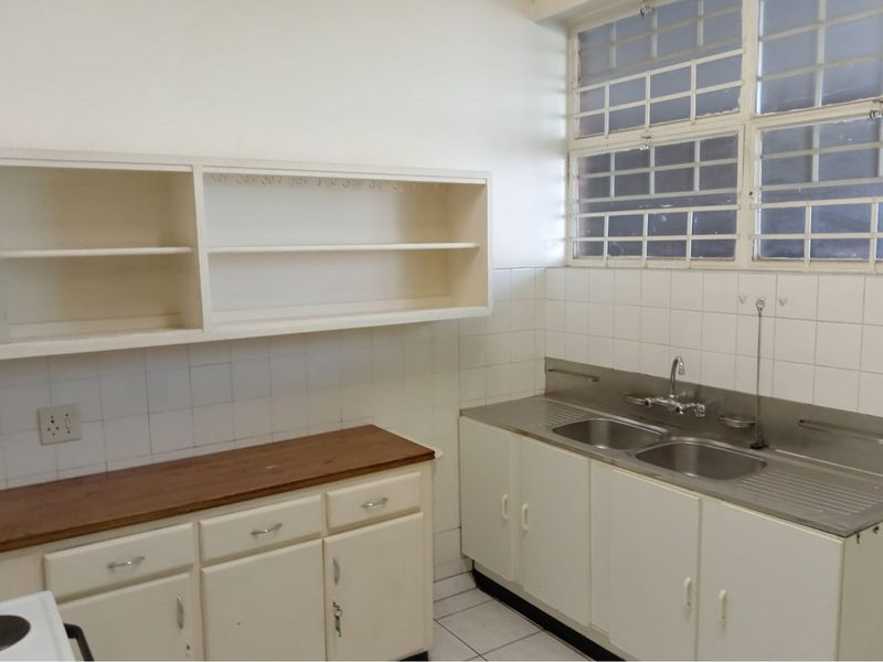 A functional, empty kitchen featuring built-in cabinetry, a double bowl stainless steel sink, tiled splashbacks, and security bars on the window.