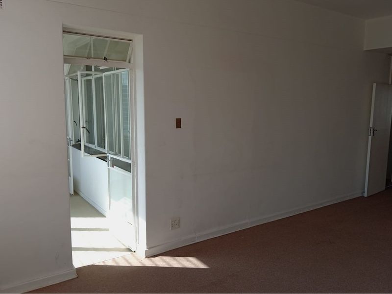 An empty living room featuring carpet flooring and access to an adjacent sunroom or balcony area.