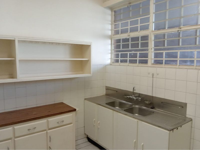 A functional scullery area featuring double stainless steel sinks, fitted cabinetry, wall-mounted shelving, and tiled splashbacks, providing practical utility space.