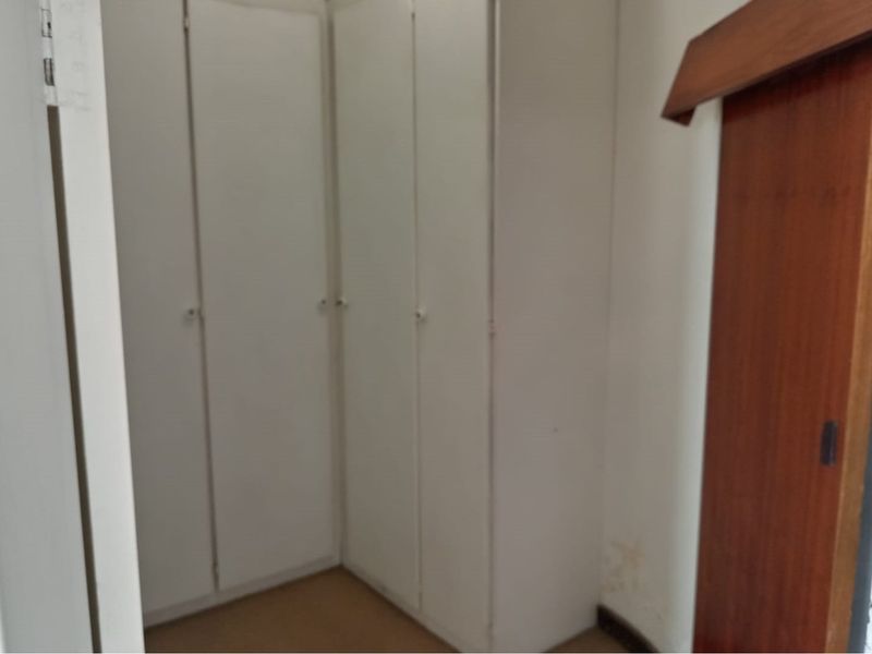 A bedroom area featuring built-in white cupboards and a wooden sliding door, showing signs of wear and wall staining.