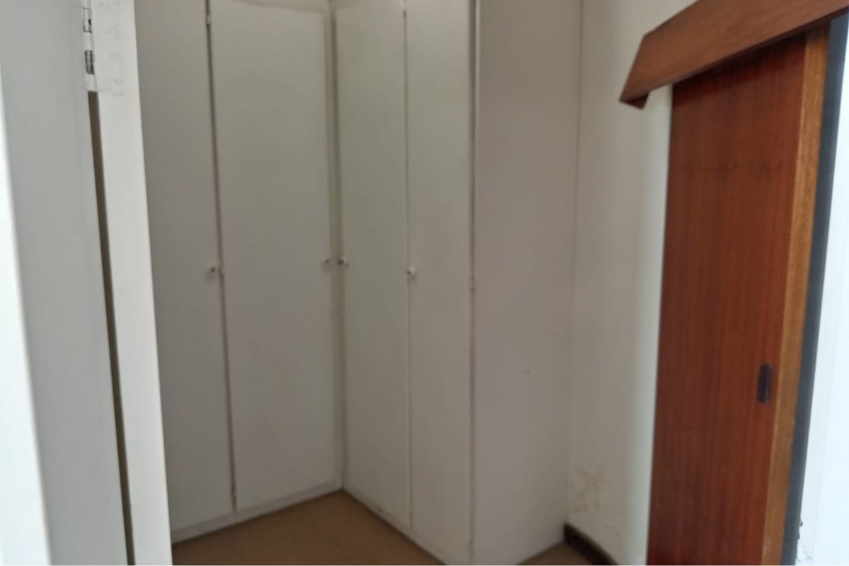 A bedroom area featuring built-in white cupboards and a wooden sliding door, showing signs of wear and wall staining.