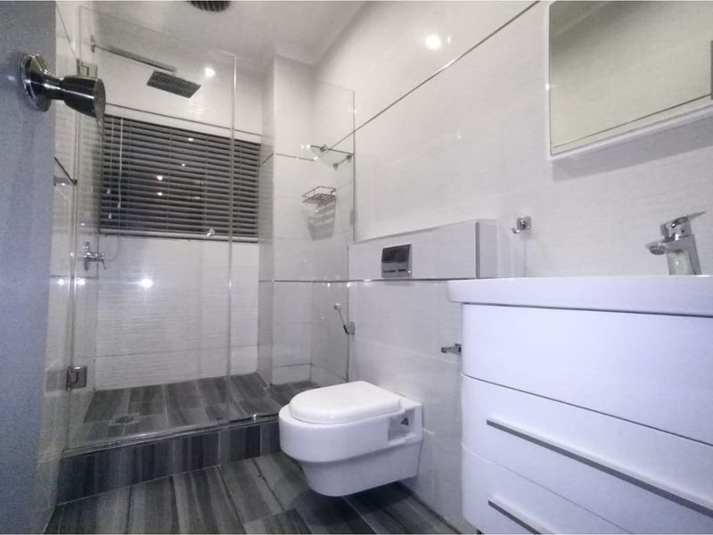 Modern bathroom featuring a wall-mounted toilet, glass-enclosed shower with a rain shower head, and a sleek vanity unit with contemporary finishes.