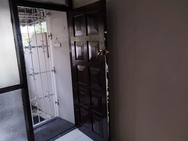 An interior view of the property entrance featuring a dark panelled door and a white metal security gate.