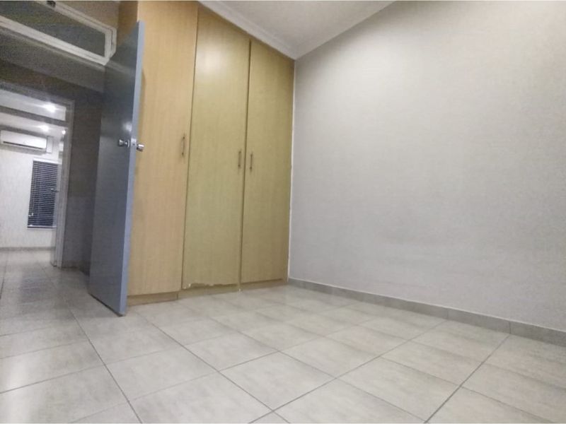 An empty bedroom featuring tiled flooring and built-in cupboards, with a view into the adjacent hallway containing an air conditioning unit.