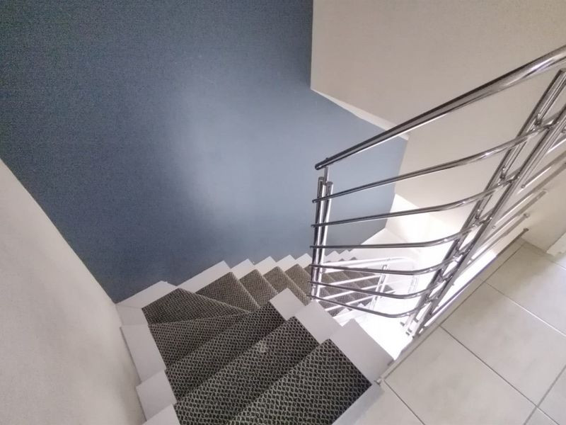 A high-angle view of a staircase featuring a modern stainless steel balustrade, carpeted steps, and neutral tiled flooring in the landing area.