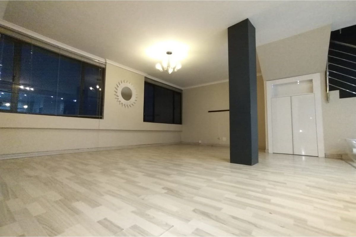 Spacious, empty living area featuring light-toned laminate flooring, a prominent structural column, and a built-in storage cupboard under the staircase.