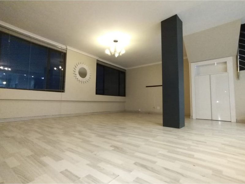 Spacious, empty living area featuring light-toned laminate flooring, a prominent structural column, and a built-in storage cupboard under the staircase.