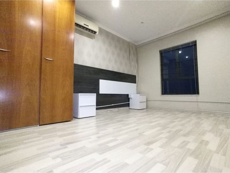 A bedroom featuring laminate flooring, a built-in wooden wardrobe, and a wall-mounted air conditioning unit.