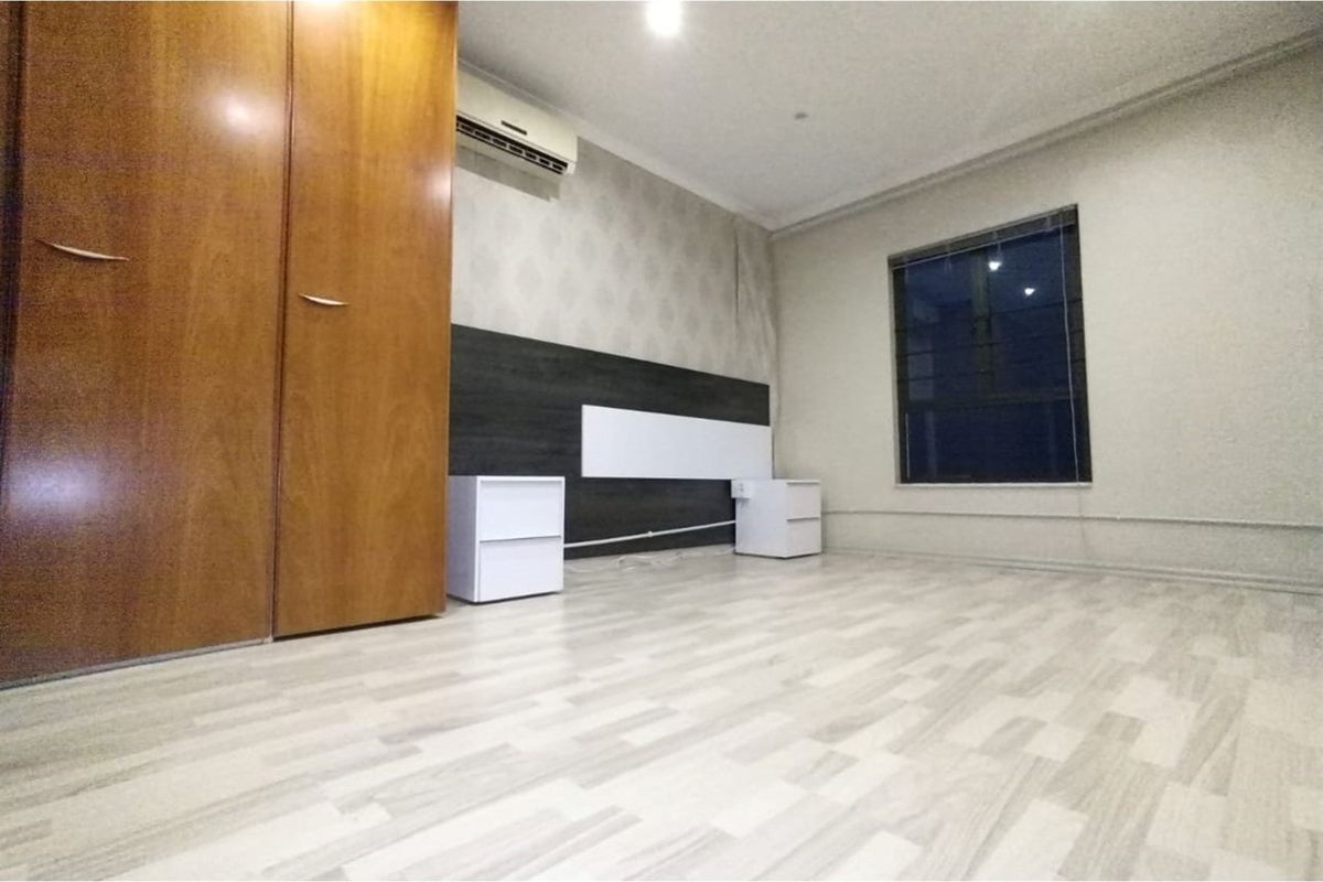A bedroom featuring laminate flooring, a built-in wooden wardrobe, and a wall-mounted air conditioning unit.