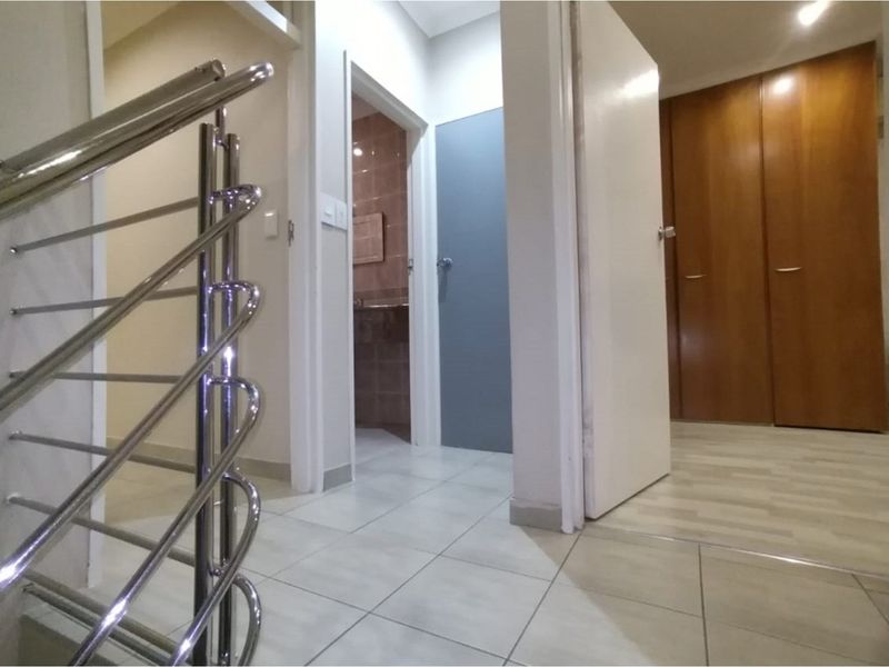 A bright hallway featuring a modern stainless steel balustrade, tiled flooring, and built-in wooden storage cupboards.