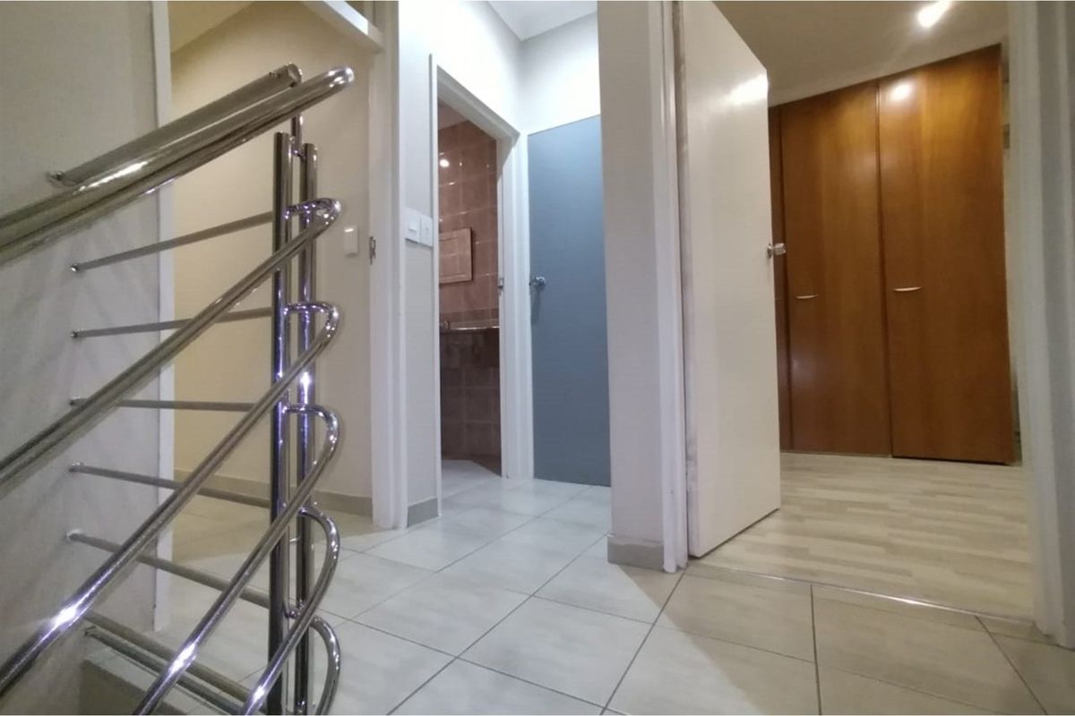 A bright hallway featuring a modern stainless steel balustrade, tiled flooring, and built-in wooden storage cupboards.