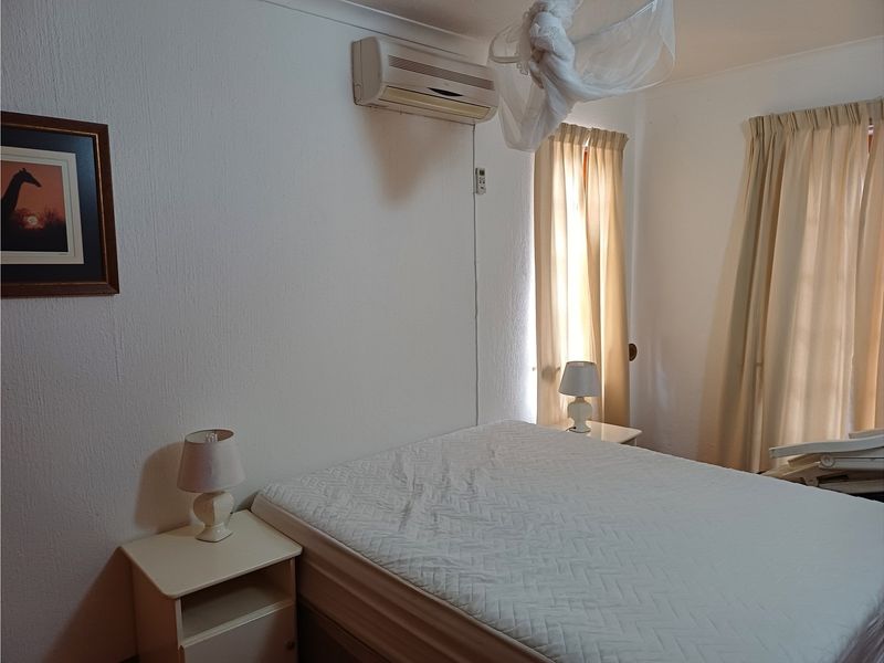 A functional bedroom featuring a wall-mounted air conditioning unit and neutral window treatments.