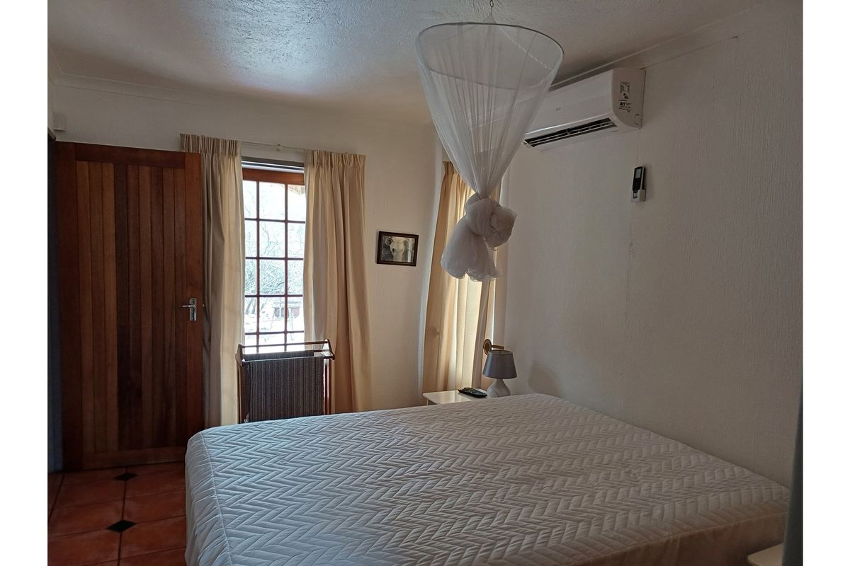 A bedroom featuring tiled flooring, a timber door, timber-framed windows, and a wall-mounted air conditioning unit.