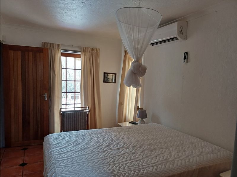 A bedroom featuring tiled flooring, a timber door, timber-framed windows, and a wall-mounted air conditioning unit.