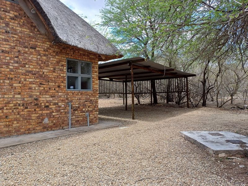 Rear exterior view of a face brick house with a thatched roof, featuring a detached carport and gravel ground cover.