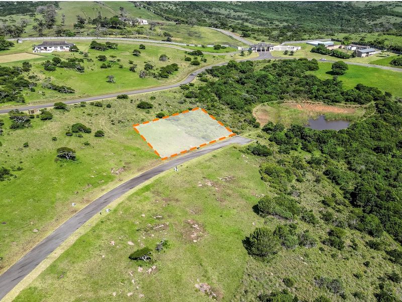 Aerial view of a vacant residential plot with road access, situated in a scenic, green estate environment.