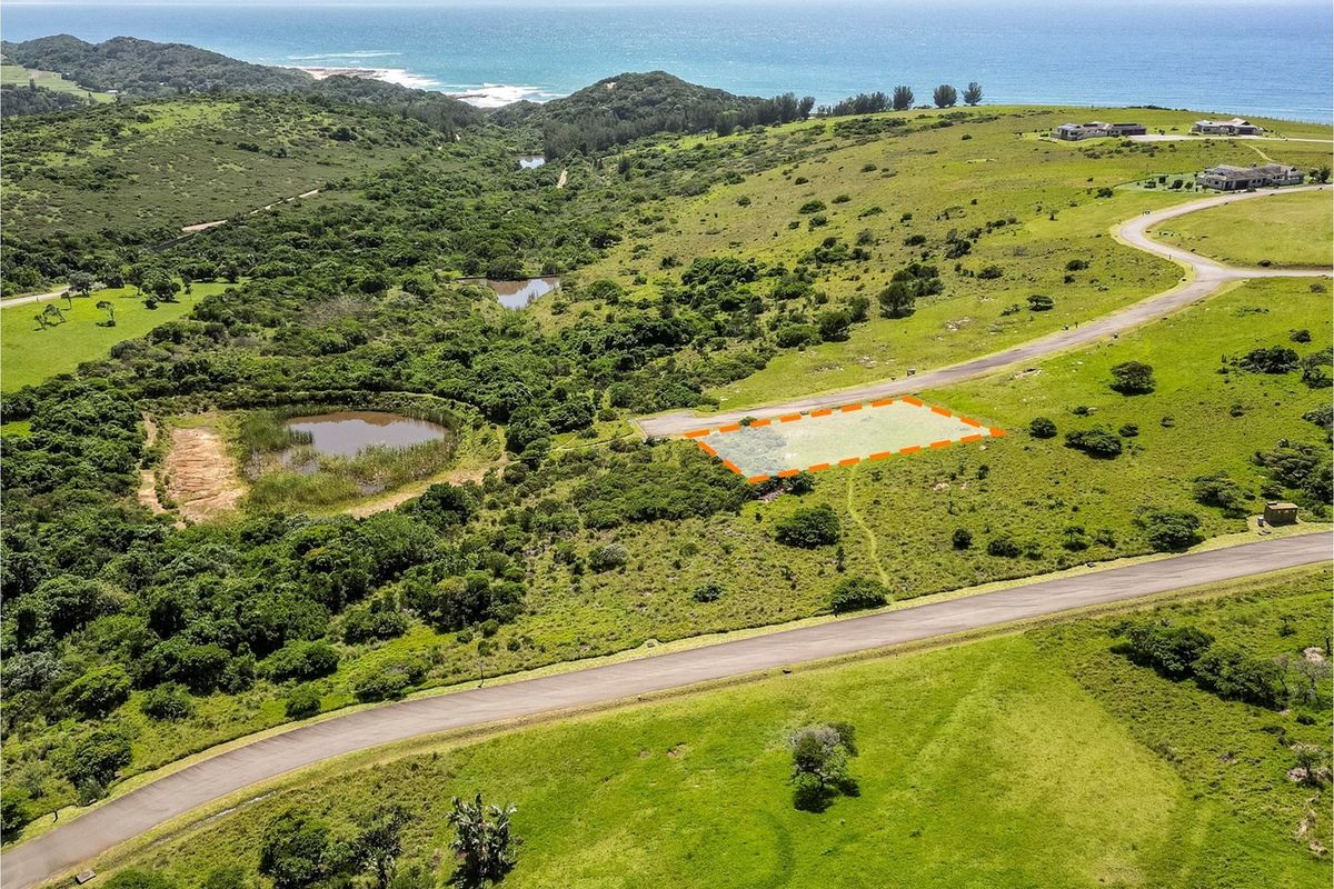 Aerial view of a vacant residential plot situated in a coastal estate, featuring paved road access and scenic natural surroundings.