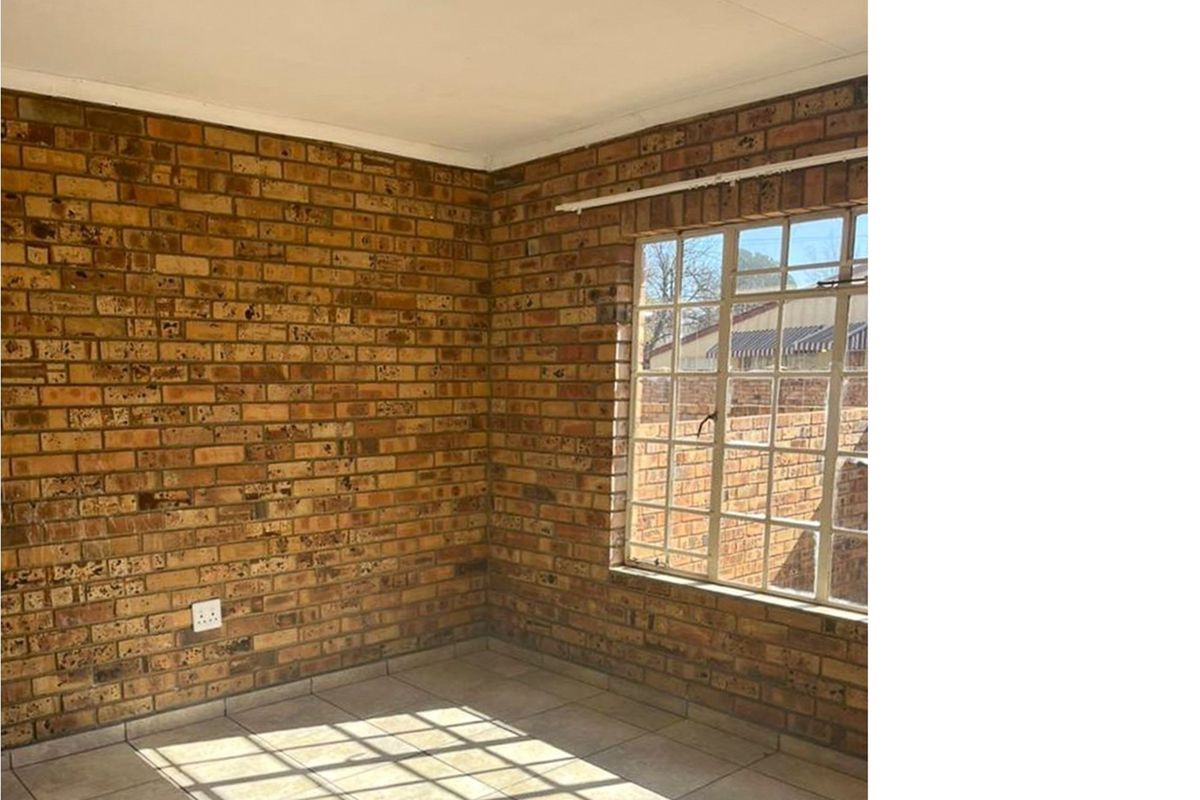 An empty bedroom featuring exposed brick walls, tiled flooring, and a large steel-framed window allowing for natural light.