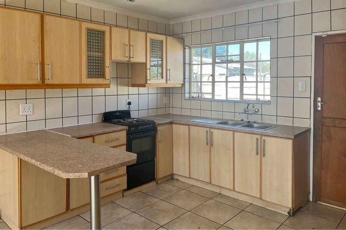 A functional kitchen featuring laminate cabinetry, a double basin sink, a freestanding stove, and tiled surfaces throughout.