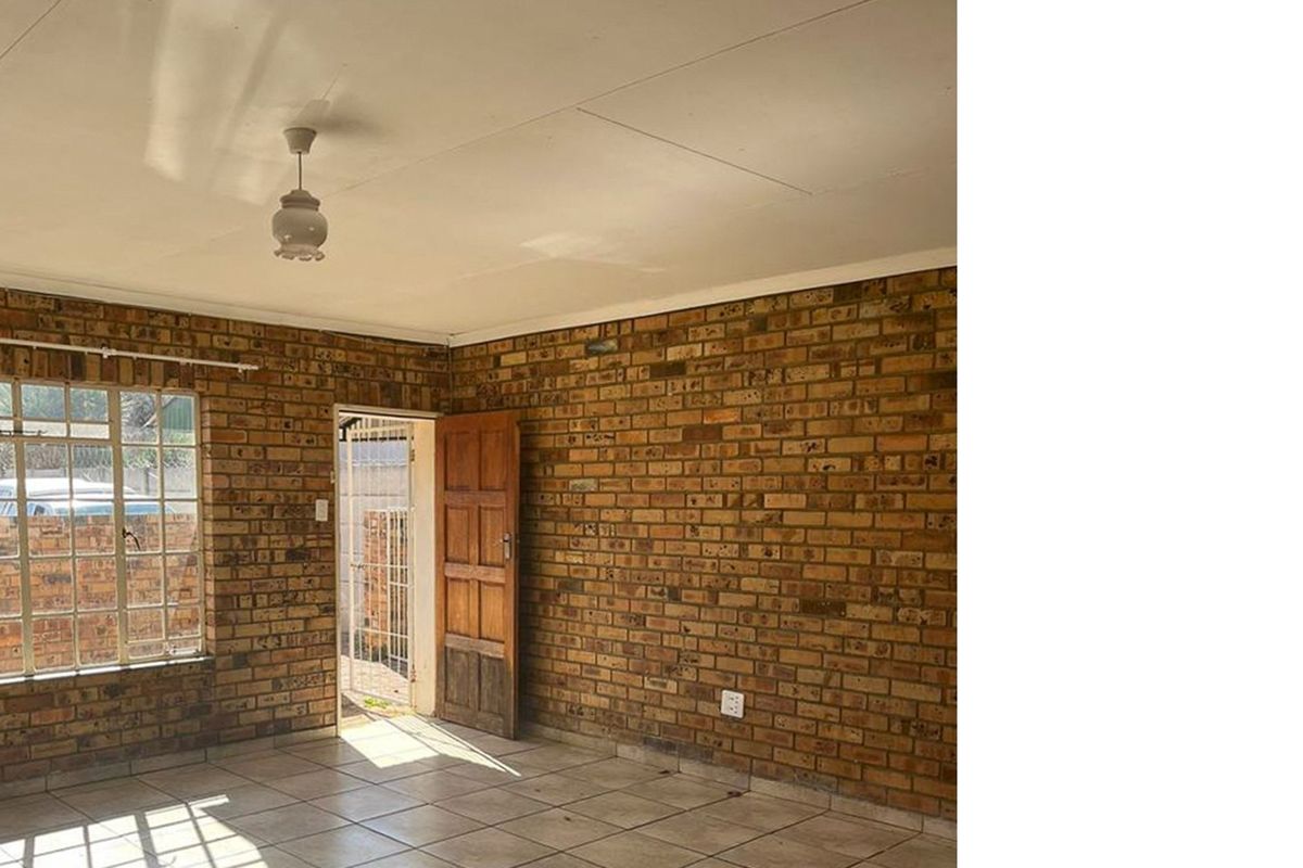 An empty living room featuring exposed brick walls, tiled flooring, and a timber door leading to an exterior area.