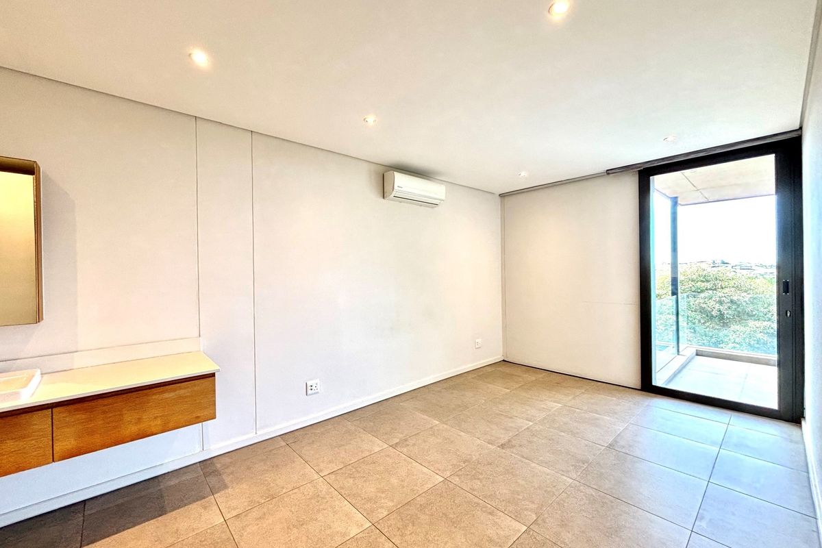 A bright, modern bedroom featuring tiled flooring, a wall-mounted vanity, integrated air conditioning, and sliding glass doors leading to a private balcony.