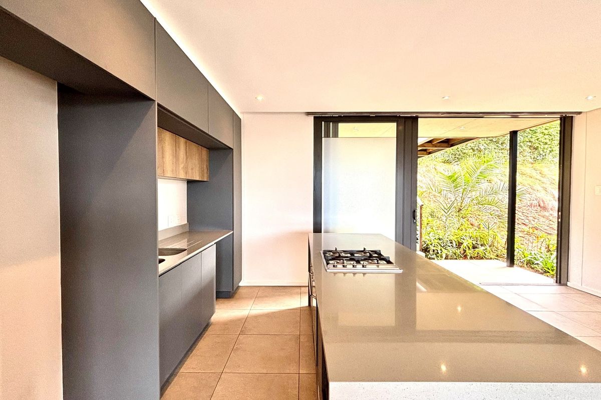 Modern kitchen featuring sleek dark cabinetry, stone countertops, a central island with a built-in gas hob, and seamless access to an outdoor patio area.